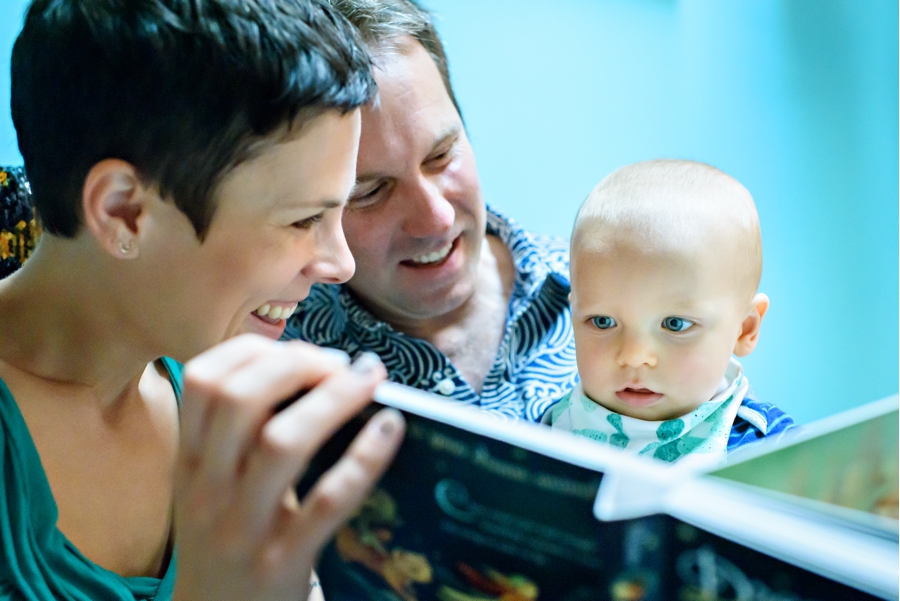 Two parents read a book to their one year old baby in thier documentary family photography session.